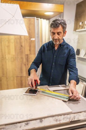 Architect taking measurements of ceramic tile using a tape measure and tablet in a home improvement store showroom