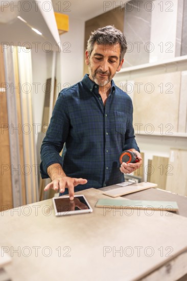 Architect using a digital tablet and choosing tiles in a home improvement store, holding a measuring tape