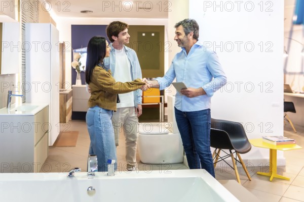 Couple shaking hands with salesman using digital tablet in bathroom furniture store, finalizing purchase agreement