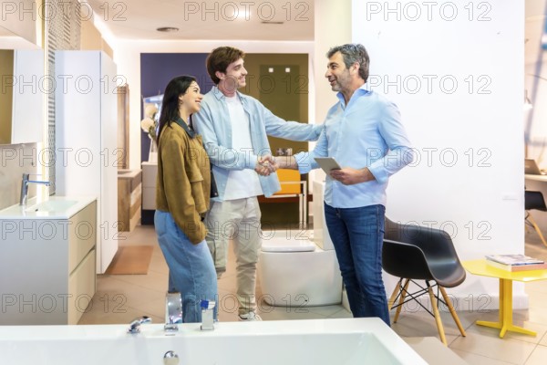 Couple shaking hands with salesman in a bathroom furniture store, finalizing purchase agreement