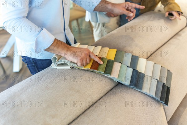 Interior designer showing fabric swatches to client, choosing upholstery for new sofa in furniture store showroom