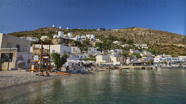 Beach promenade on a clear blue sea, behind it Mediterranean town and windmills on hill, Pandeli Castle, Leros Castle, St John's Fortress, Apitiki Hill, Pandeli Bay, Agia Marina, Leros, Dodecanese, Greek Islands, Greece