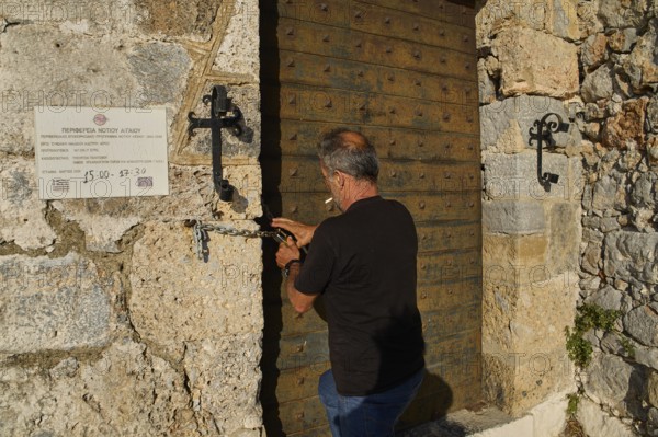 Man opens antique, massive wooden gate in stone wall, Pandeli Castle, Castle, Leros Fortress, St John's Fortress, Apitiki Hill, Pandeli Bay, Windmills, Leros, Dodecanese, Greek Islands, Greece