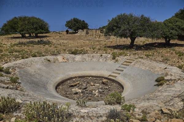Crater in an arid environment with trees and stony ground under a blue sky, Lost Place, Air Defence Position, Aerophone, Parabolic Acoustic Mirror, Patella Mountain, WW2, west of Lakki, Leros, Dodecanese, Greek Islands, Greece