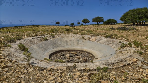 Dry terrain with a crater and scattered trees under a clear sky, Lost Place, Air Defence Position, Aerophone, Parabolic Acoustic Mirror, Patella Mountain, WW2, west of Lakki, Leros, Dodecanese, Greek Islands, Greece