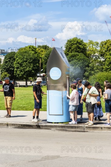 A queue of people in front of a drinking water fountain in the city centre of Vienna, Austria