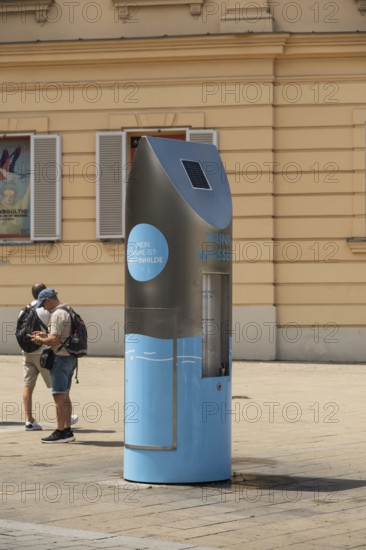 Two people in front of a drinking water fountain in the city centre of Vienna, Austria