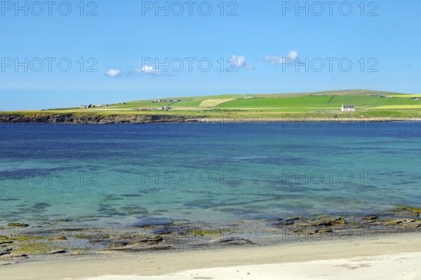 Clear blue sky over a coastal landscape with green shore and crystal clear water, Skara Brae, Neolithic settlement, Mainland, Orkney Islands, Scotland, United Kingdom