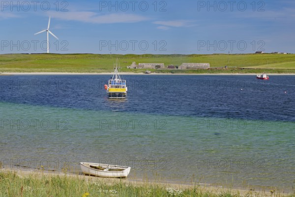 Colourful coastal landscape with boat, windmill and vast water under blue sky, Lambholm, Orkney Islands, Scotland, Great Britain