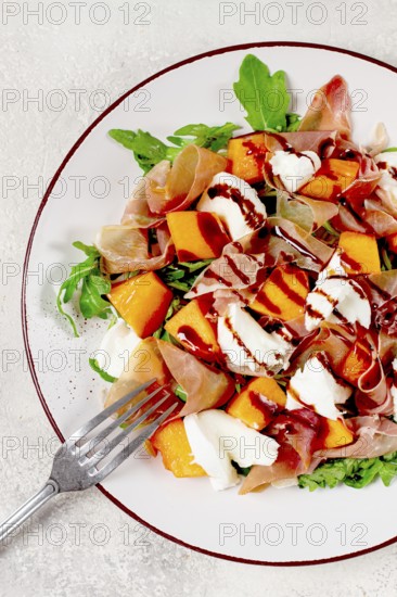 Salad with slices of ripe melon, prosciutto, mozzarella and fresh arugula, decorated with balsamic glaze