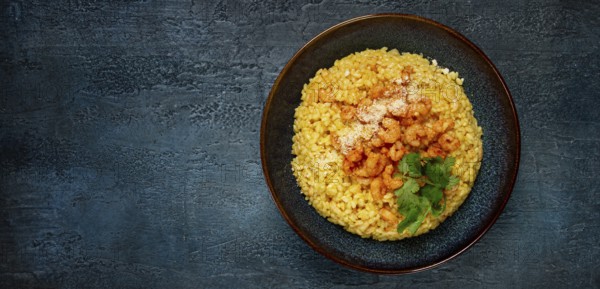 Risotto with shrimp, in a bowl, on a textured surface, with a side dish of fresh coriander, homemade, no people