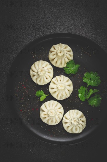 Khinkali, a traditional Georgian dish, with spices and herbs, top view, no people, on a black plate