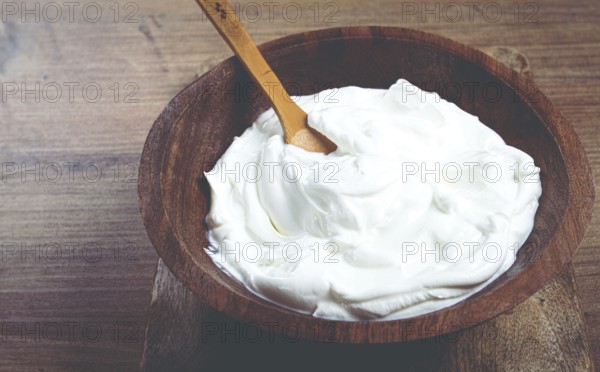 Sour cream in a wooden bowl, on a wooden table, top view, close-up, no people