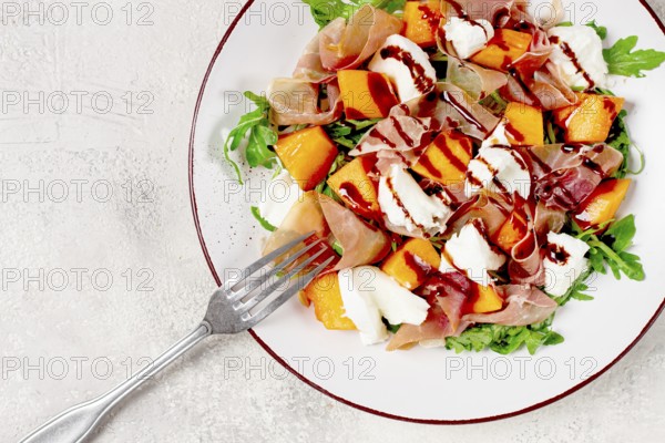 Salad with slices of ripe melon, prosciutto, mozzarella and fresh arugula, decorated with balsamic glaze