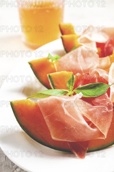 Cantaloupe melon with prosciutto and fresh basil, on a white plate, natural light
