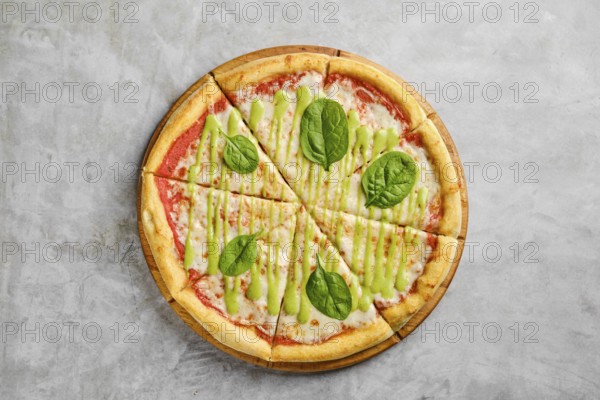 Mouthwatering pizza features a golden crust topped with rich tomato sauce, melted cheese, and fresh spinach leaves drizzled with a vibrant green sauce. Perfect for a casual meal at any time