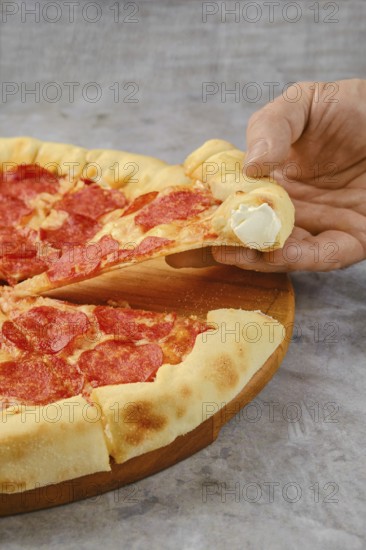 Delicious pepperoni pizza on a wooden board with a hand reaching for a slice. The crust is golden brown, and cheese is stretching, revealing a gooey interior