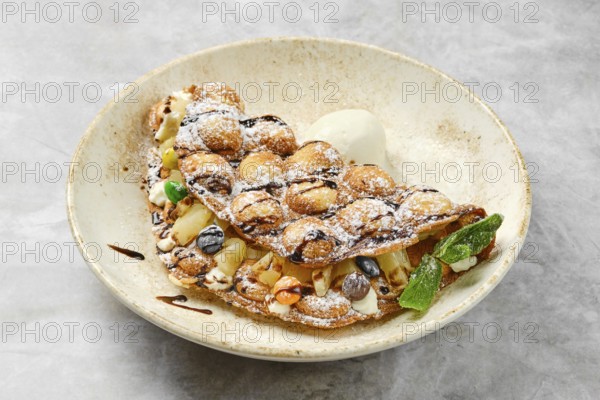 A mouthwatering dessert showcases a fluffy, golden-brown waffle filled with a variety of fresh fruits, cream, and drizzled chocolate. It sits elegantly in a rustic bowl, inviting indulgence