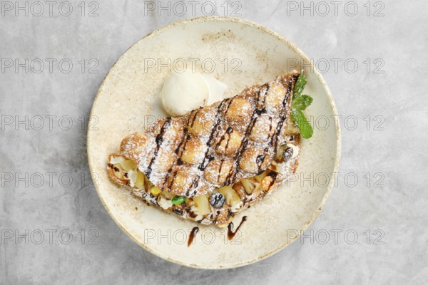 A beautifully plated dessert showcases a waffle filled with a variety of fresh fruits, drizzled with chocolate sauce and dusted with powdered sugar