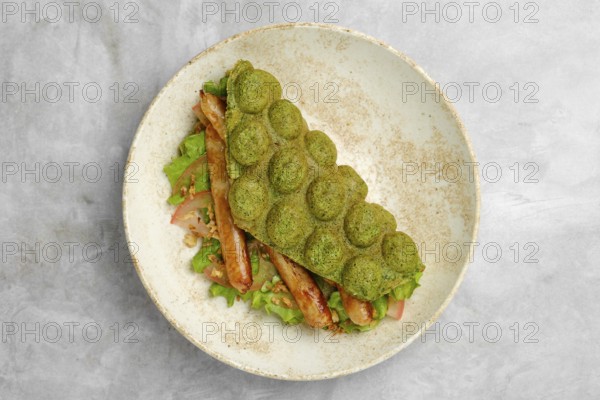 A creatively served sandwich features a green waffle made from spinach, filled with grilled sausage and fresh lettuce