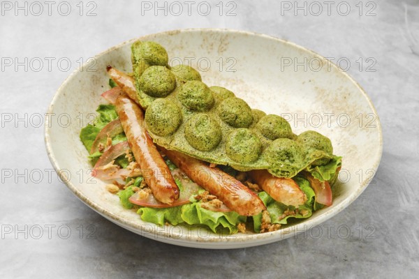 A vibrant green waffle is placed atop a bed of fresh lettuce, featuring tender grilled sausage and colorful vegetables. This dish highlights creative culinary presentation and freshness