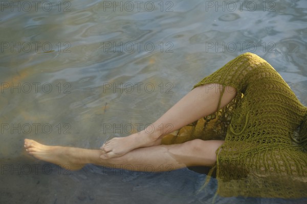 On a warm day, a person relaxes by the lake, dipping her feet into the clear water. Sunlight dances on the surface, creating a tranquil atmosphere ideal for summer enjoyment and relaxation