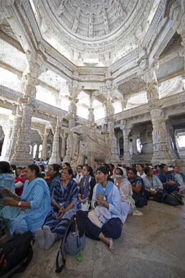 Indian woman pray between the white marble pillars around a marble elephant statue in the Adinath temple in Ranakpur, Jain temple, Rajasthan, India