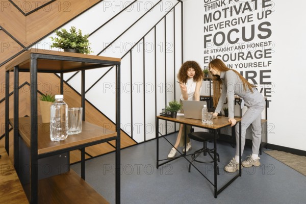 Two women are bent over a laptop and studying a prototype of their health monitoring program