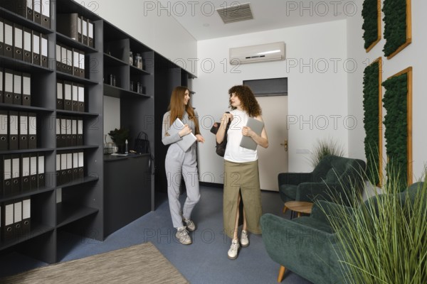 Two women engage in a lively conversation about women's health initiatives in a stylish office filled with greenery and organized files, showcasing a supportive workplace culture