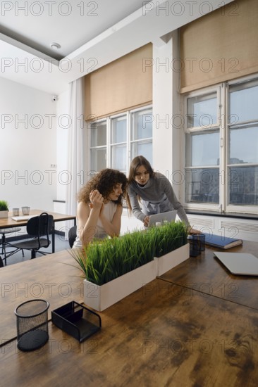 In a modern workspace, two women engage in a focused discussion about women's health initiatives. They share ideas while examining documents and prototype application