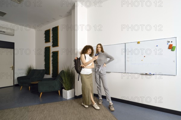 At the end of a productive working day in coworking, two women called a taxi online and look at the screen of a smartphone