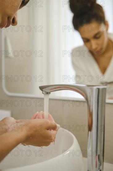 In a contemporary bathroom, a woman is washing her hands under a sleek faucet. She focuses on her hygiene while preparing for her day. Natural light fills the space, creating a serene atmosphere