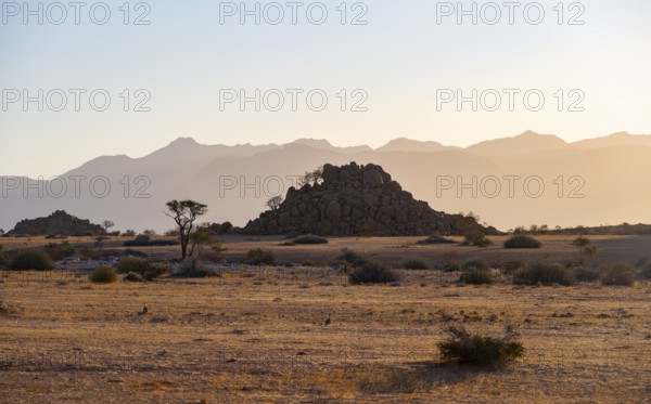 Desert landscape in the evening light at sunset, barren landscape with hills of stacked rocks, backlit, Brandberg in the background, Erongo, Damaraland, Namibia