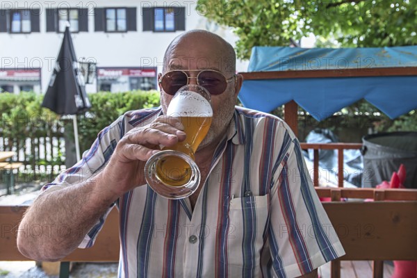 Senior citizen with sunglasses drinking a wheat beer in a beer garden, Upper Bavaria, Germany