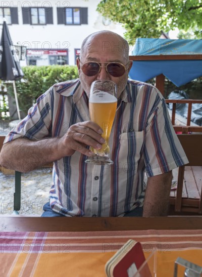 Senior citizen with sunglasses drinking a wheat beer in a beer garden, Upper Bavaria, Germany
