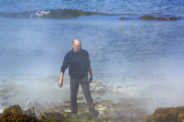 Hot spring flows into the sea, tourist on steaming rocky coast near Reykjanes, Súðavík, Ísafjarðardjúp fjord, Vestfirðir, Westfjords, Iceland