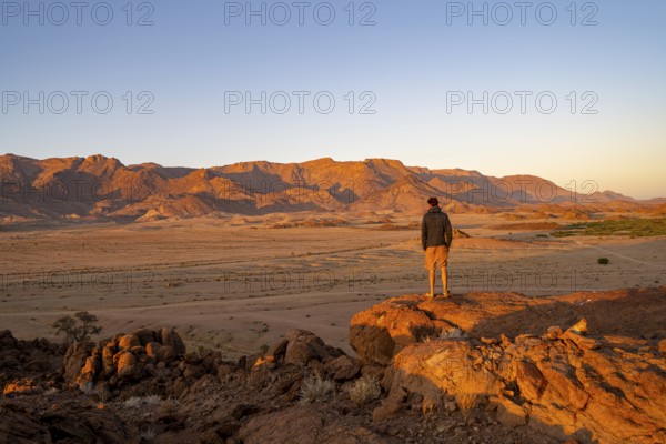 Young man in dry desert landscape, Brandberg in the morning light, at sunrise, Erongo, Damaraland, Namibia
