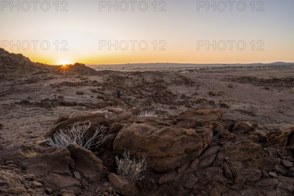 Photographer in desert landscape at sunrise with sun star, Erongo, Damaraland, Namibia