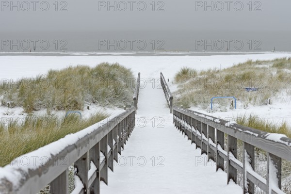 Winter day, onset of winter, wooden plank path leads through the snow-covered dune landscape to the North Sea, Norddeich, Lower Saxony, Germany