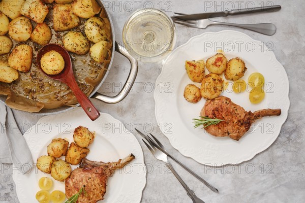 A delicious roasted pork rib roast is served alongside golden, crispy potatoes on elegant plates. The inviting meal is perfect for a gathering or special occasion, complemented by a glass of wine