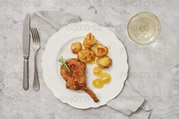 A delicious roasted pork rib roast is plated alongside golden, seasoned potatoes. The dish is garnished with a sprig of fresh herbs, creating an appetizing presentation perfect for a special meal