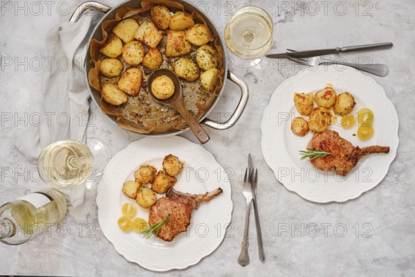 Pork rib roast paired with crispy golden potatoes on white plates. Enjoy this inviting meal set on a dining table with glasses of white wine