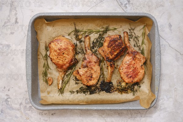 Juicy pork rib roasts are seasoned and cooked to perfection on a baking tray lined with parchment paper. Fresh herbs add flavor, creating an appetizing dish suitable for any occasion