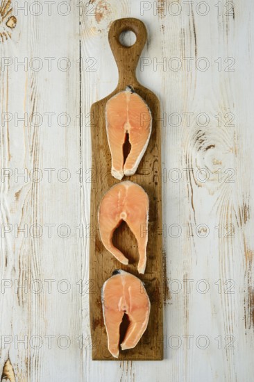 Three slices of fresh salmon steaks cross cut are arranged on a rustic wooden cutting board