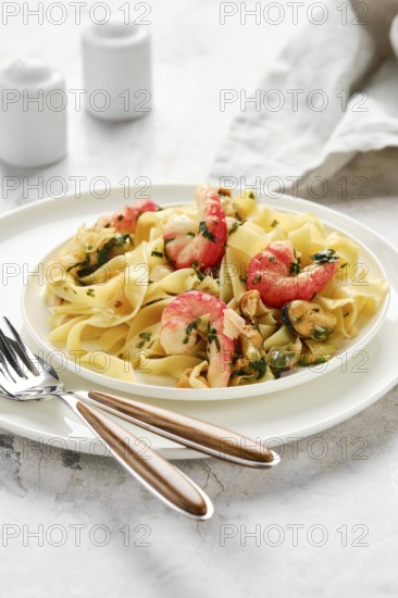 A delectable portion of fettuccine allo scoglio sits elegantly on a white plate. The dish features seafood such as shrimp and mussels, garnished with fresh herbs