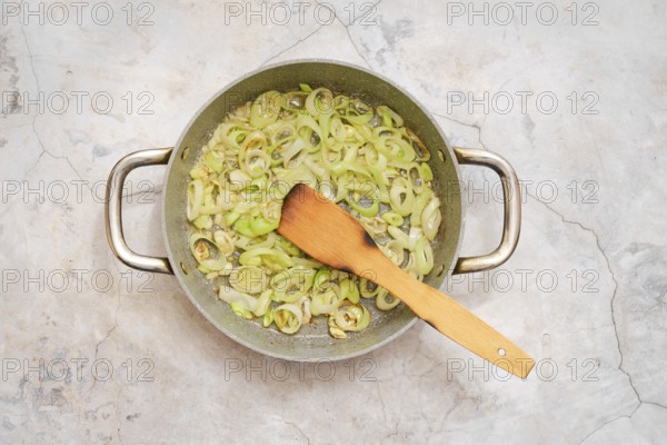 A pot filled with sautéed leek is on a countertop, showcasing a mix of fresh flavour being prepared for fettuccine allo Scoglio. A wooden spatula rests inside, ready for stirring