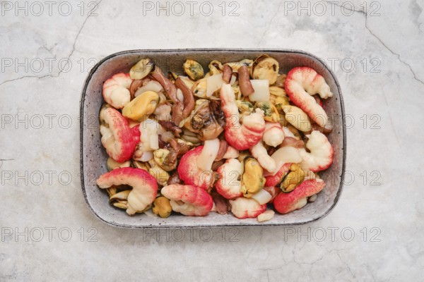 Overhead view of a bowl with shrimps, mussels, and squid. The dish showcases vibrant colors and fresh ingredients, perfect for a flavorful experience by the coast at dinner time