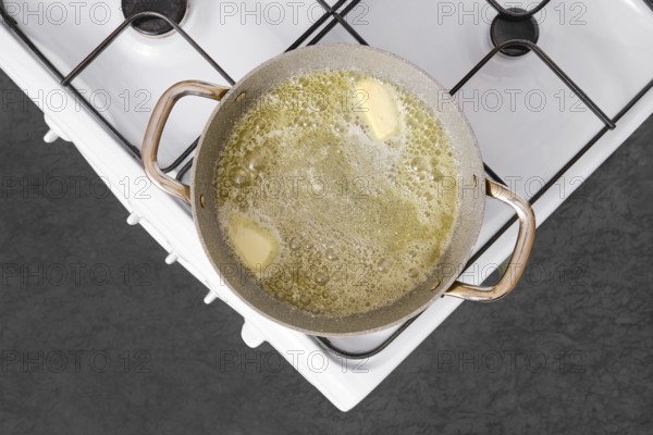 A pot on a stove is filled with melted butter, bubbling as it simmers. This is the starting point for preparing fettuccine allo scoglio, a flavorful seafood pasta dish