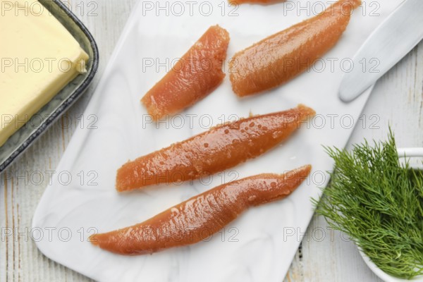 Herring caviar are neatly arranged on a marble cutting board alongside a block of butter and fresh dill