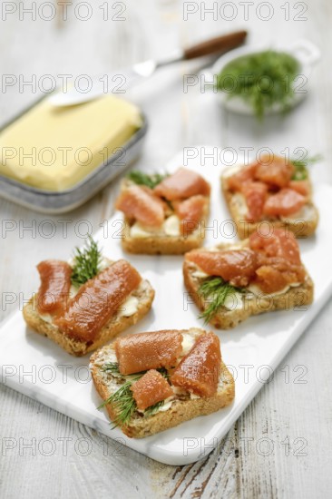 Pieces of toasted bread are topped with herring caviar and garnished with fresh herbs, arranged neatly on a white platter. Variation of open face sandwich